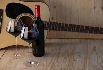 Acoustic guitar, bottle and glasses of red wine on wooden table. Space for text