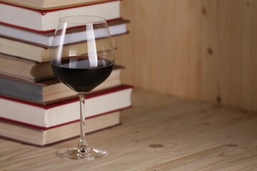 Glass of red wine and stacked books on wooden table, closeup. Space for text