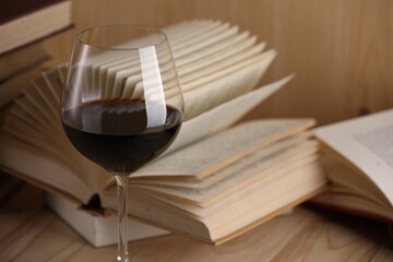 Glass of red wine and open books on wooden table, closeup