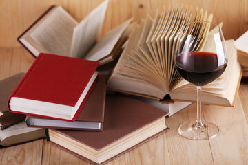 Glass of red wine and books on wooden table, closeup