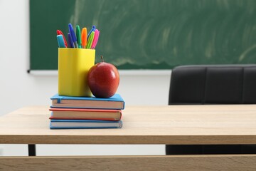 Different school stationery and red apple on wooden table near blackboard indoors, space for text