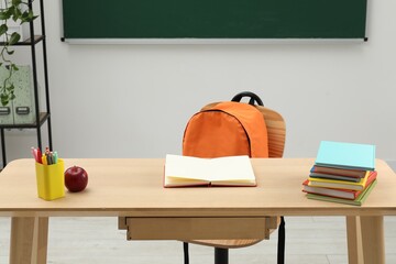 Different school stationery and red apple on wooden table near blackboard indoors