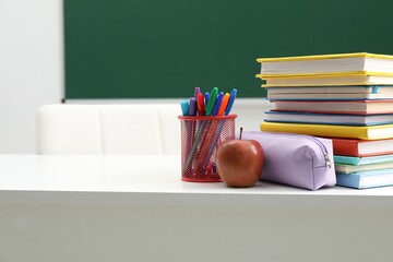Different school stationery and apple on white table near blackboard indoors, space for text
