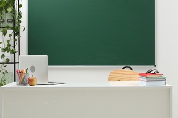 Different school stationery, laptop, glasses and apple on white table near blackboard indoors