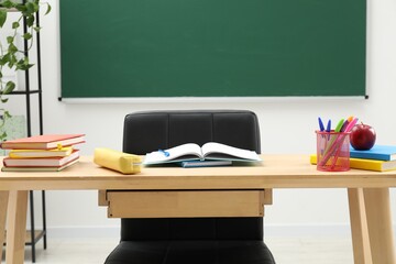Different school stationery and red apple on wooden table near blackboard