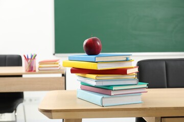 Different books and red apple on wooden table indoors