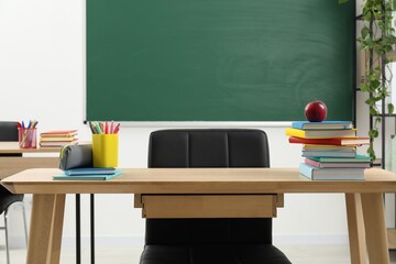 Different school stationery and red apple on wooden table near blackboard indoors