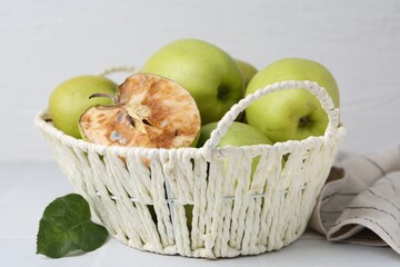 Spoiled apple and good ones in basket on white table, closeup