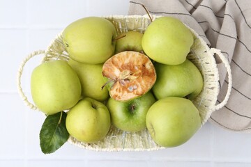 Spoiled apple and good ones in basket on white table, top view