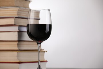 Red wine in glass and stack of books on light background, closeup. Space for text