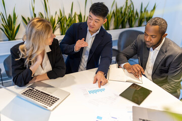 Multiethnic business team sitting at desk collaborating on project with laptop and documents