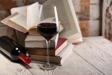 Red wine in glass, bottle and books on light table against color wooden background, closeup