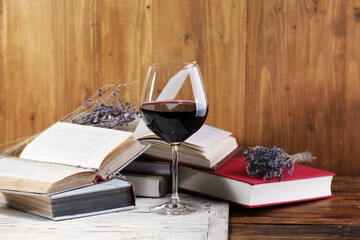 Red wine in glass, lavender flowers and books on wooden table, closeup