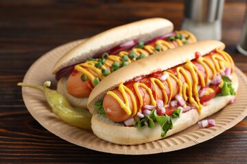 Delicious hot dogs with sauces, lettuce and onion on wooden table, closeup