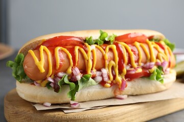 Delicious hot dog with sauces, lettuce, onion and tomato on grey table, closeup