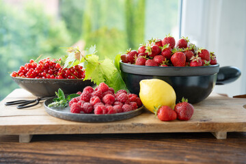 Freshly picked organic summer fruits. Ripe himbeeren, erdbeeren und currants dekorated on rustic wood against bright sunny background. Close-up of healthy seasonal fruits.