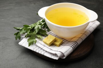 Aromatic bouillon cubes, broth and parsley on black table, closeup