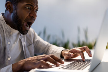 Astonished male employee typing quickly on laptop and looking at screen with surprised expression