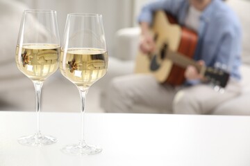 Glasses with white wine on table and man playing guitar indoors, selective focus