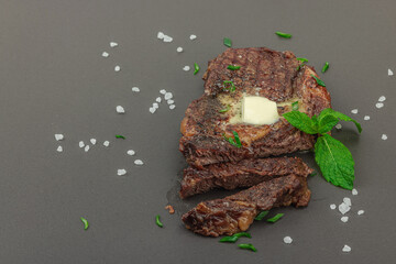 Grilled ribeye steak with melted butter and herbs on dark background, high protein meal concept