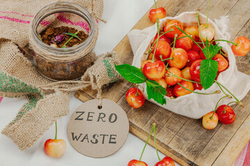 Sweet ripe cherries in a cotton bag on rustic wooden board, next to a compost jar with dried flower