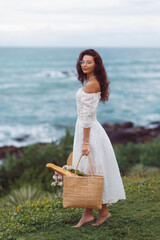 Elegant Woman in White Dress Holding Picnic Basket by the Ocean View