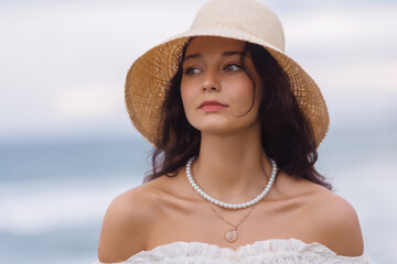 Elegant Woman in Straw Hat and White Dress with Ocean in Background