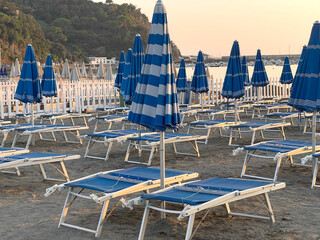 Blue beach umbrellas and sunbeds near sea against blue sky. Summer and vacation in Liguria, Italy. Background for text.