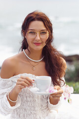 Stylish Woman in Glasses Enjoying Tea Outdoors in White Lace Dress