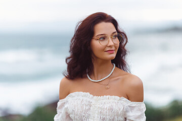 Elegant Woman in White Dress Wearing Pearls and Glasses by the Sea