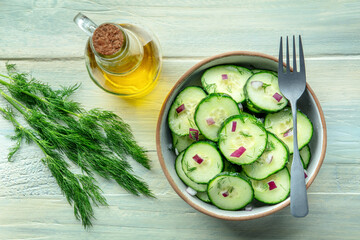 Cucumber salad with olive oil, dill and red onion, shot from the top on a rustic wooden background, with a fork
