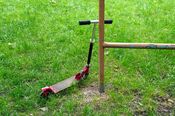 Red scooter on the grass leans against an iron pipe
