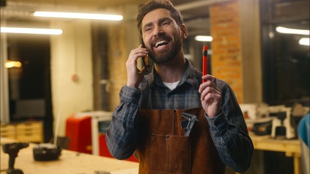 Cheerful glad Caucasian guy builder wood master craftsman man talking mobile phone conversation designer artist repairman cellphone call with client carpenter work art in workshop carpentry male speak