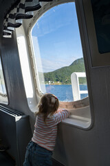 Little girl enjoying a water view by the window during a trip by ferry between islands in Norway.