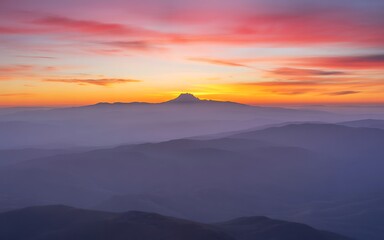 Dramatic sunset paints the sky with vibrant colors over a hazy mountain silhouette