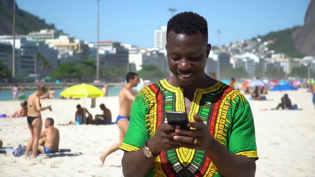 Smiling African man in traditional Dashiki shirt using a smartphone on a crowded sunny beach