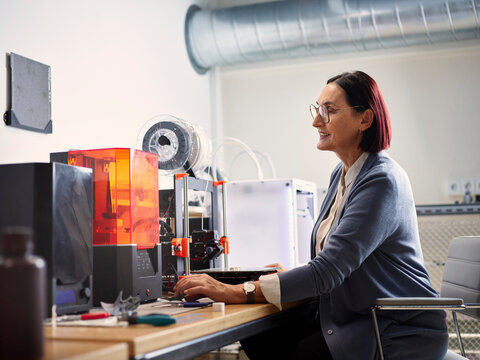 Smiling mature technician operating SLA printer on desk at workshop