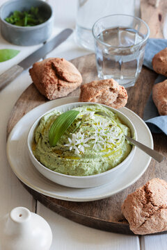 Wild garlic dip with herb cream cheese and bread rolls on a wooden board