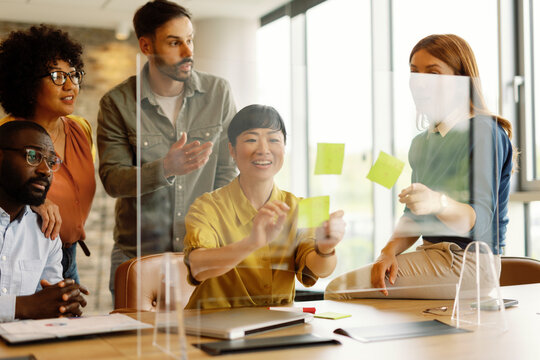 Office team brainstorming in a modern workspace with post-it notes on a glass board - Powered by Adobe