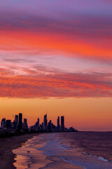 Red and orange colours in the sky over Gold Coast Australia, with surfer on the beach.