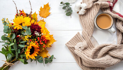 a top down shot displays a seasonal, cozy scene on a white surface. a vibrant bouquet with sunflowers, leaves, and berries is tied together in the lower left corner