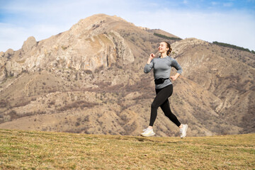 A young woman trail runner cross country running to the high altitude mountain peak, jogging along...