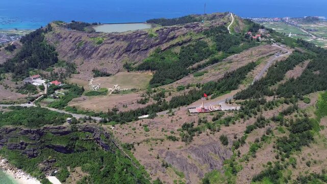 Zoom out revealing rocky volcanic cliffs, rural buildings and sea in Ly Son Island, Vietnam on a sunny afternoon.