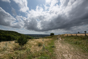 A peaceful rural scene showing a hillside path under a cloudy sky, with open views across the...