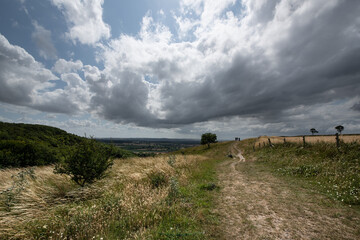 A peaceful rural scene showing a hillside path under a cloudy sky, with open views across the...