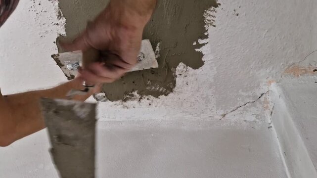 Close-up of male hands applying a layer of repair adhesive to a damaged ceiling using a masonry trowel and float. The renovation takes place in an old building