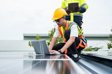 Asian solar technician using laptop to monitor photovoltaic system performance on rooftop under...