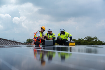 Group of solar engineers in safety gear discussing installation plans on rooftop, using laptop and...