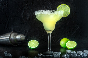 Margarita cocktail in the classic glass, side view on a black background, with ice. Summer drink...