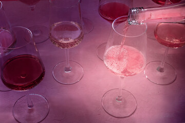 Pink wine poured from a bottle into a glass at a wine tasting, on a pink background, with shadows